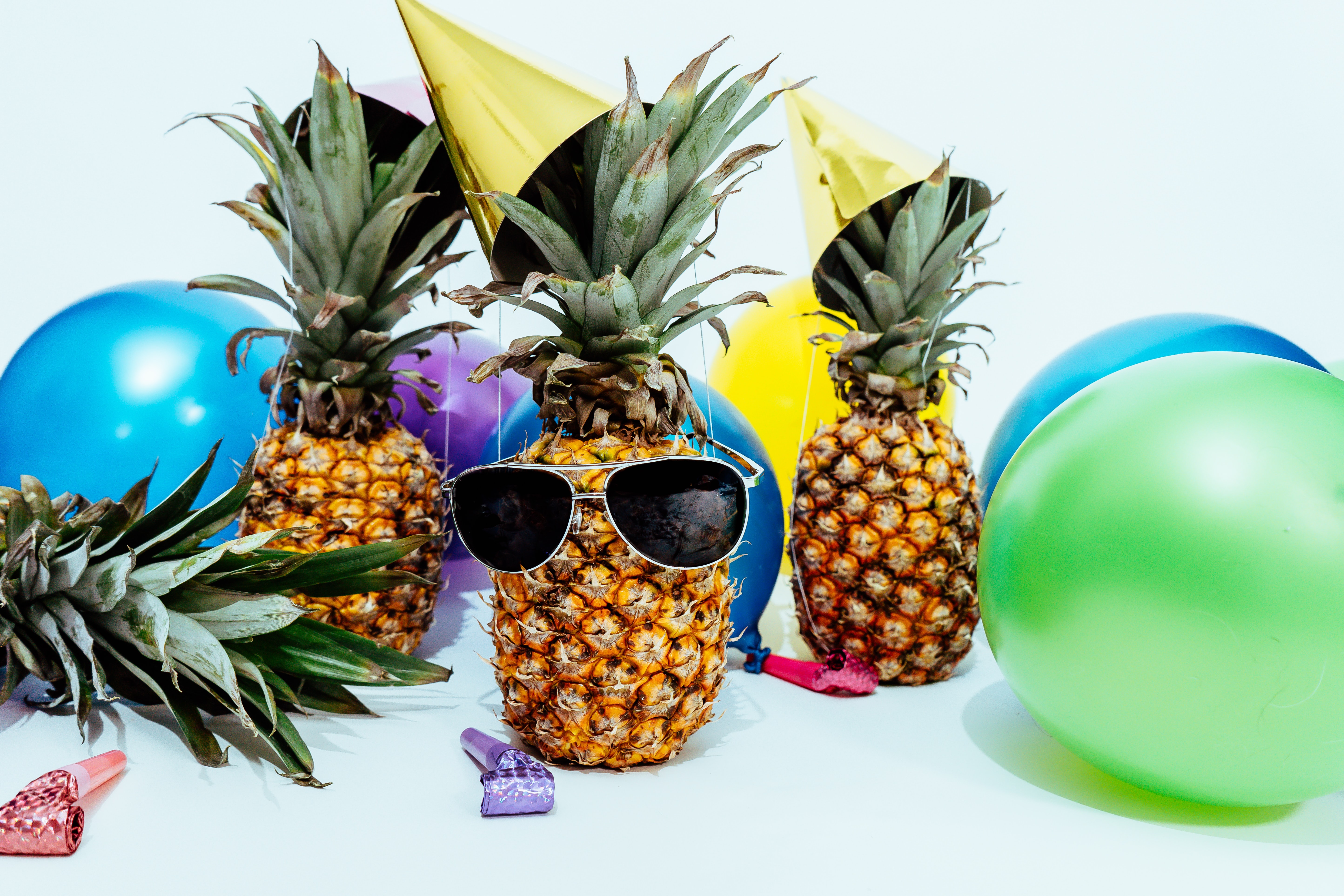 pineapples with party hats and sunglasses and balloons